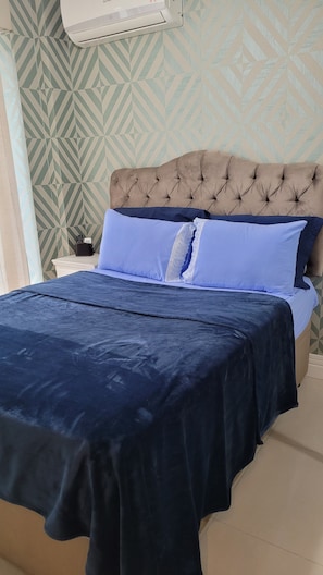 A bed with a tufted headboard, a dark blue bedspread, and light blue pillows. - New Listing (Petrópolis)