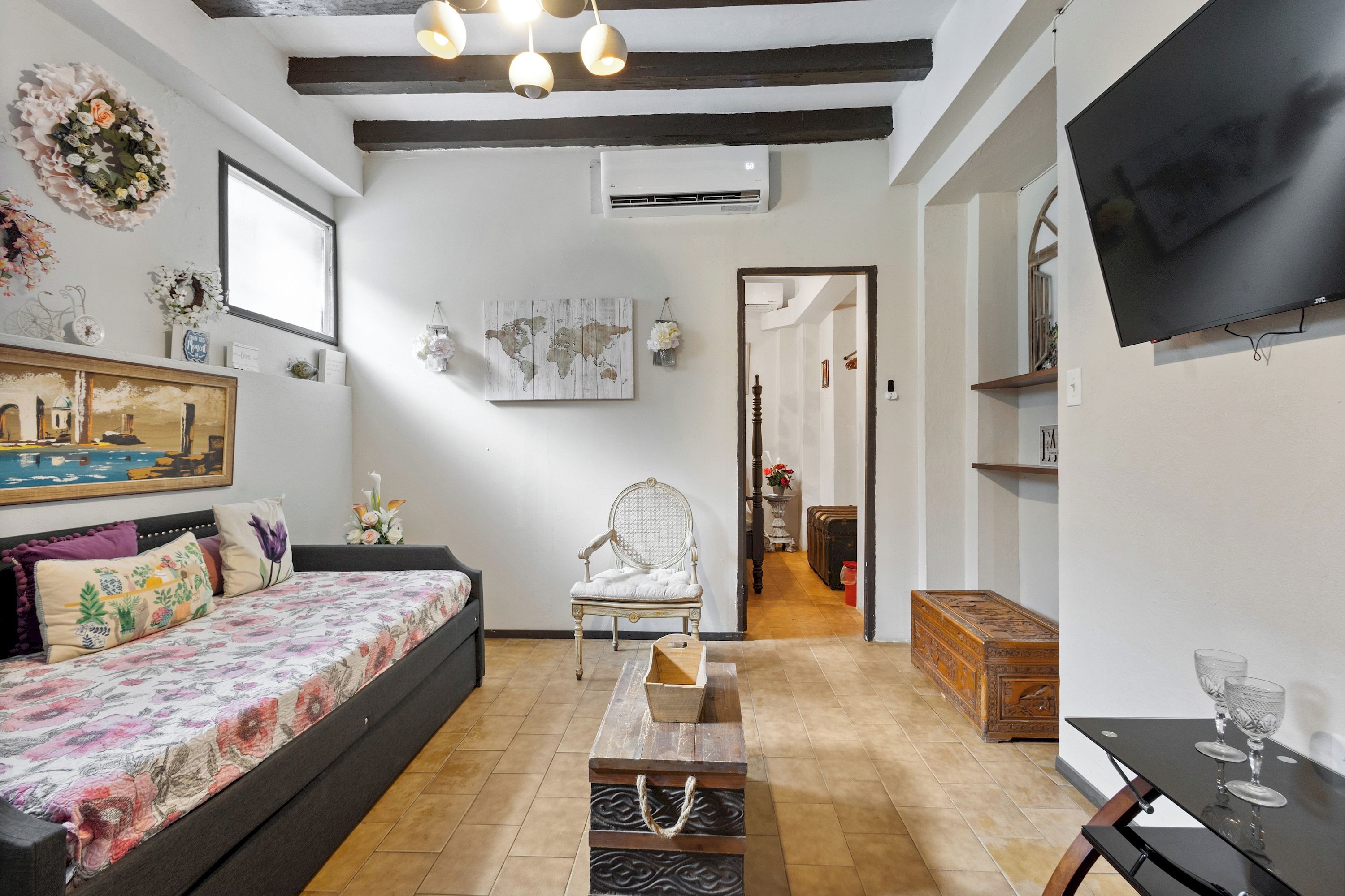 Una sala de estar amoblada con un sofá, una mesa de centro de madera, un sillón decorativo, un televisor de pantalla plana y un mapa del mundo en la pared.