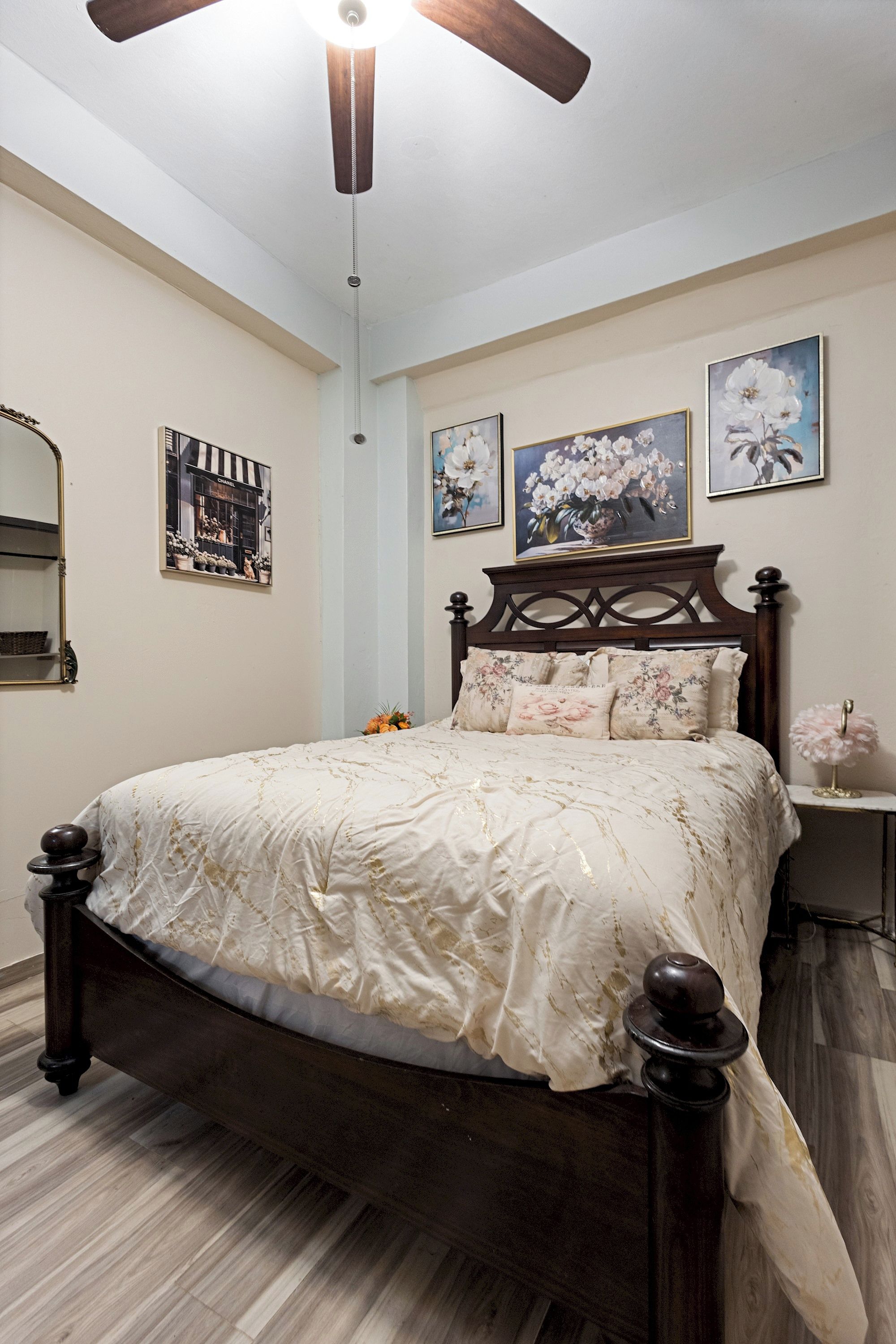 Un dormitorio con estructura de cama de madera, ventilador de techo y decoración floral en la pared.