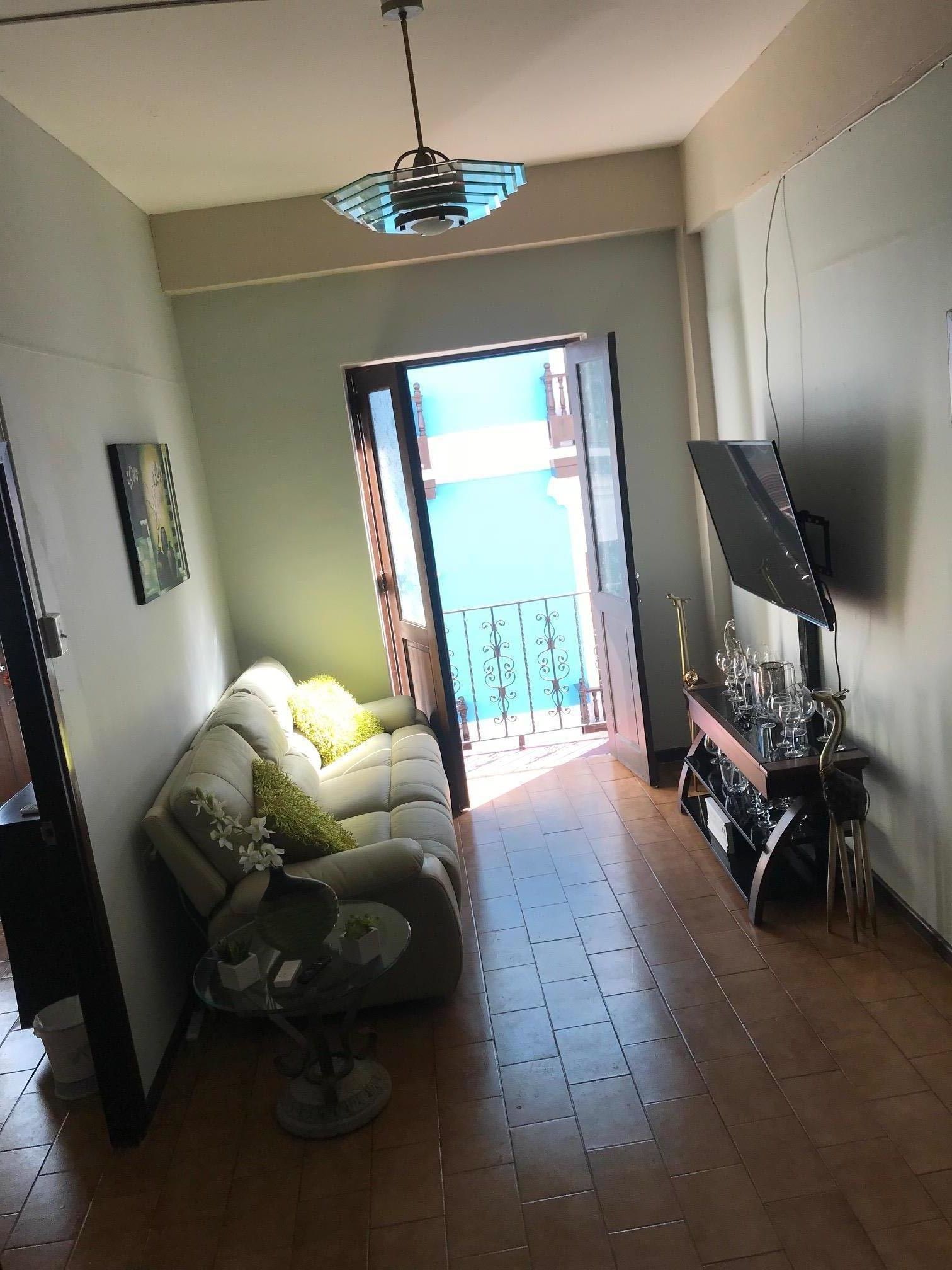 Una sala de estar con sofá, mesa de centro, televisor y un balcón con barandilla.