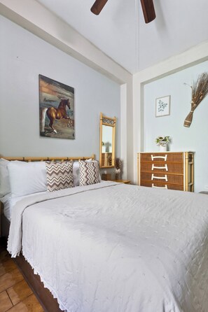 A bedroom with a large bed, a wooden dresser, a mirror, and a painting on the wall. - The Bambu Room at Casa of Essence | Old San Juan Comfort (San Juan)