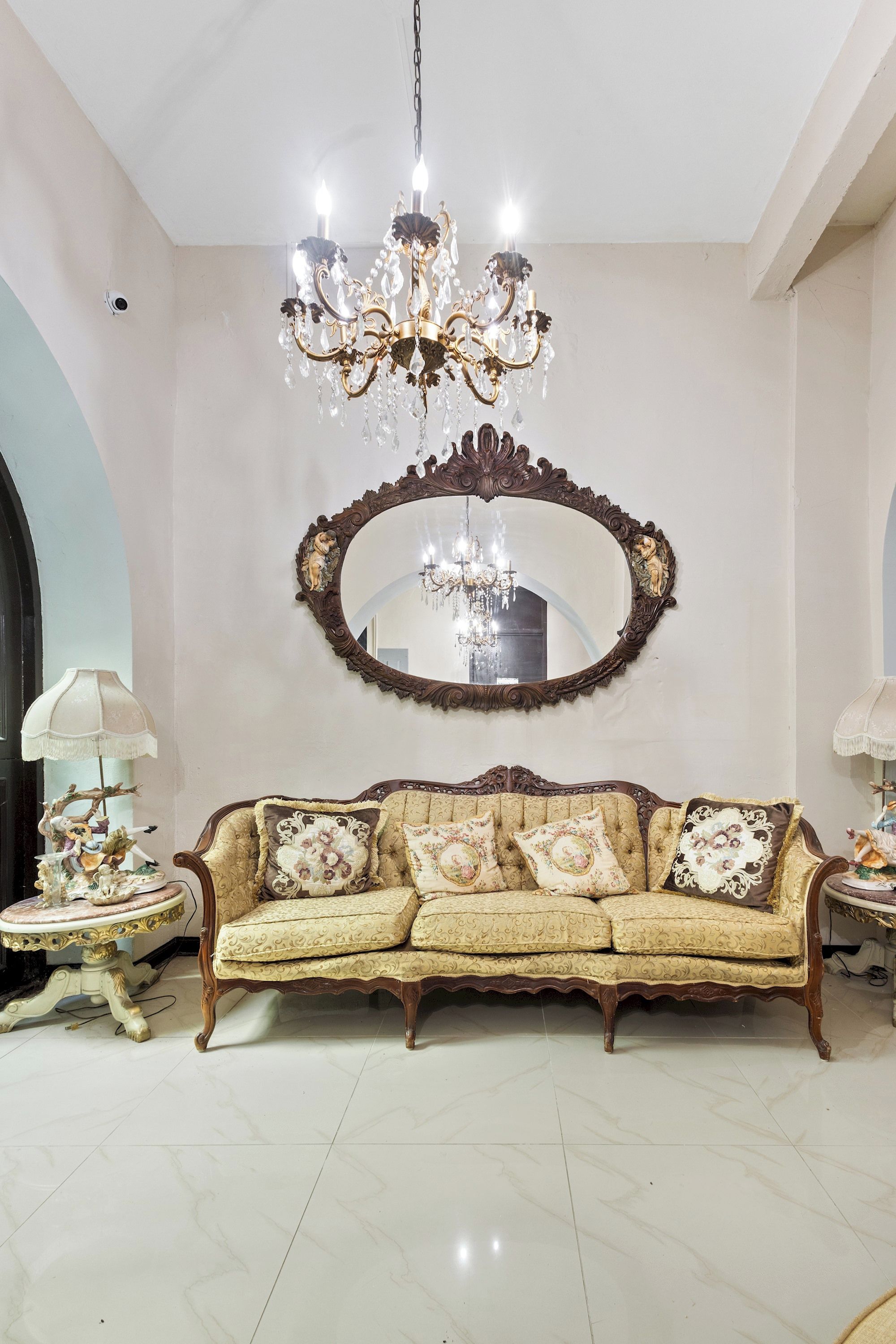 Una habitación con un sofá grande y ornamentado, un candelabro y un espejo con un marco elaborado.