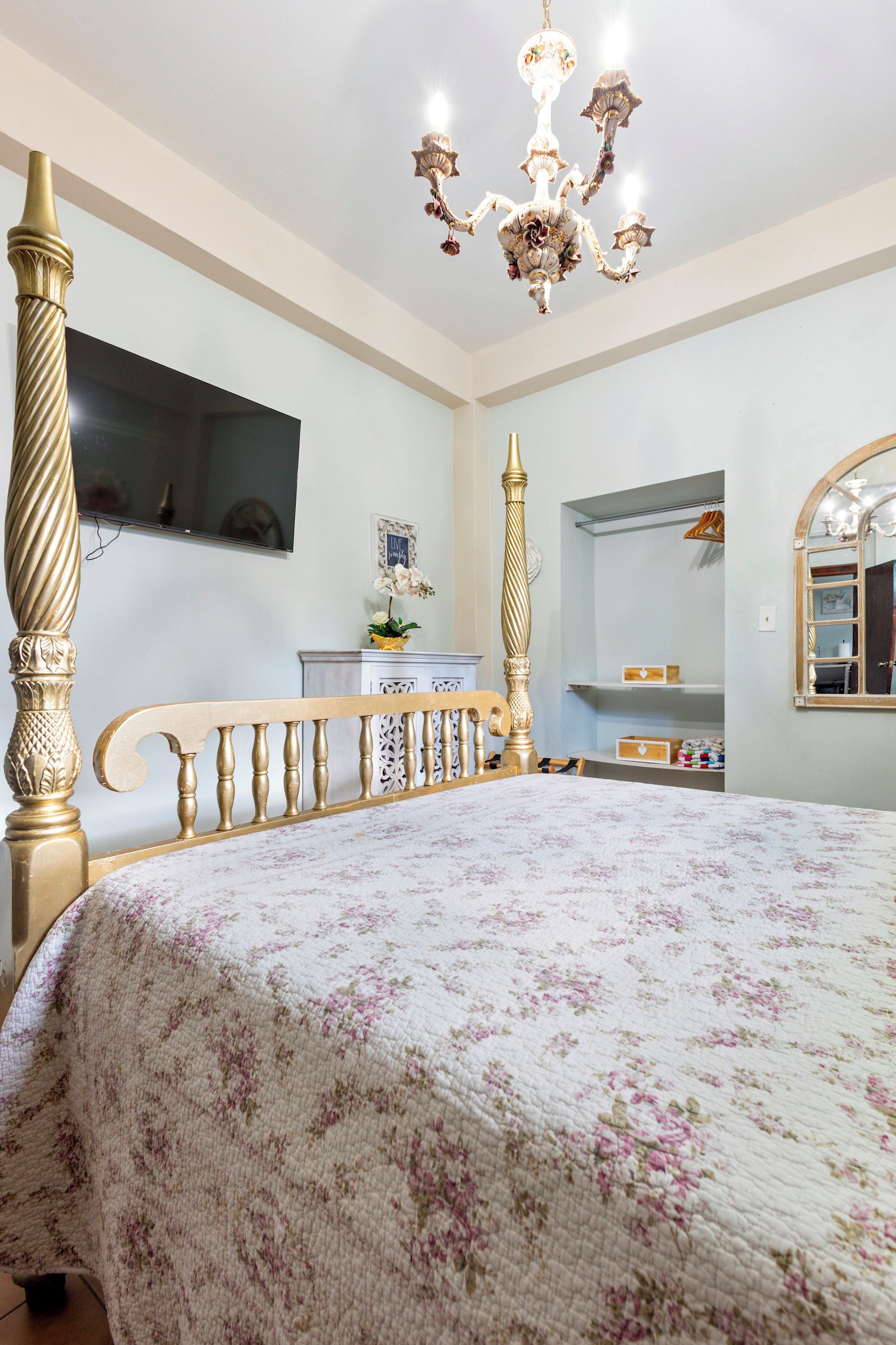 Un dormitorio con una cama con dosel, un candelabro, un televisor y un espejo.
