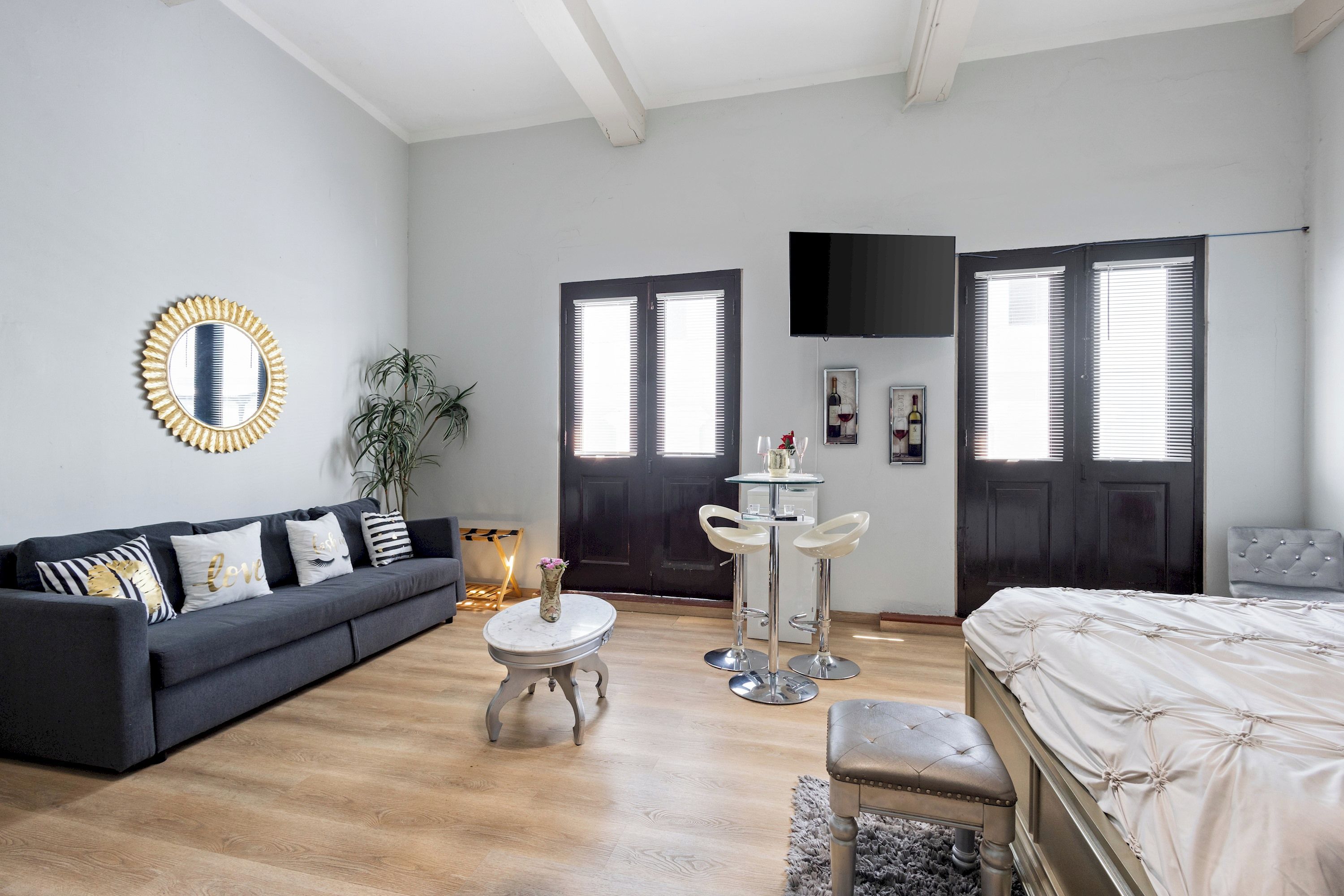 Un dormitorio moderno con un sofá gris oscuro, una cama blanca y una mesa redonda con dos taburetes de bar.