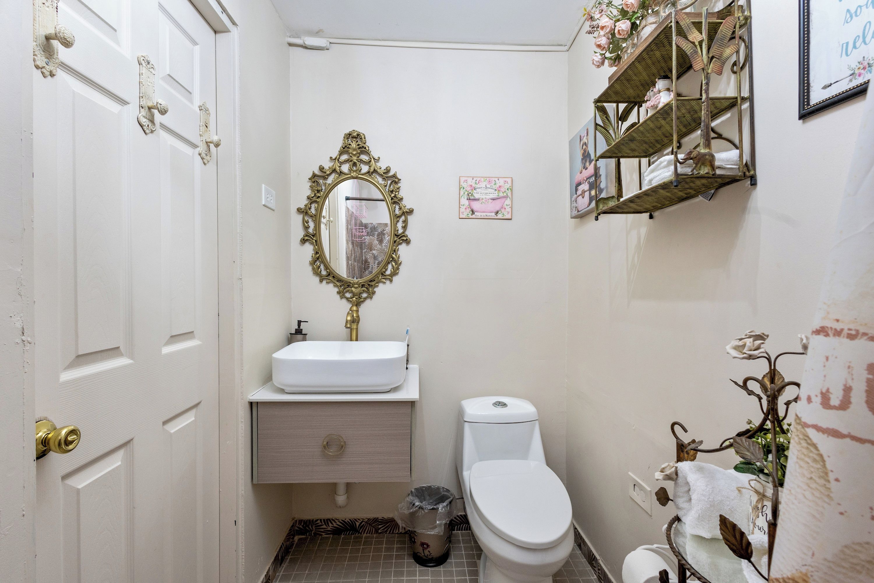 Un baño con un lavabo blanco, un inodoro, un espejo decorativo y una repisa con artículos de aseo.
