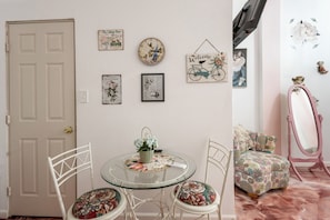 Une pièce avec une porte, une table ronde en verre entourée de chaises, un mur orné de divers tableaux encadrés, un miroir et un canapé agrémenté de coussins à motifs.
