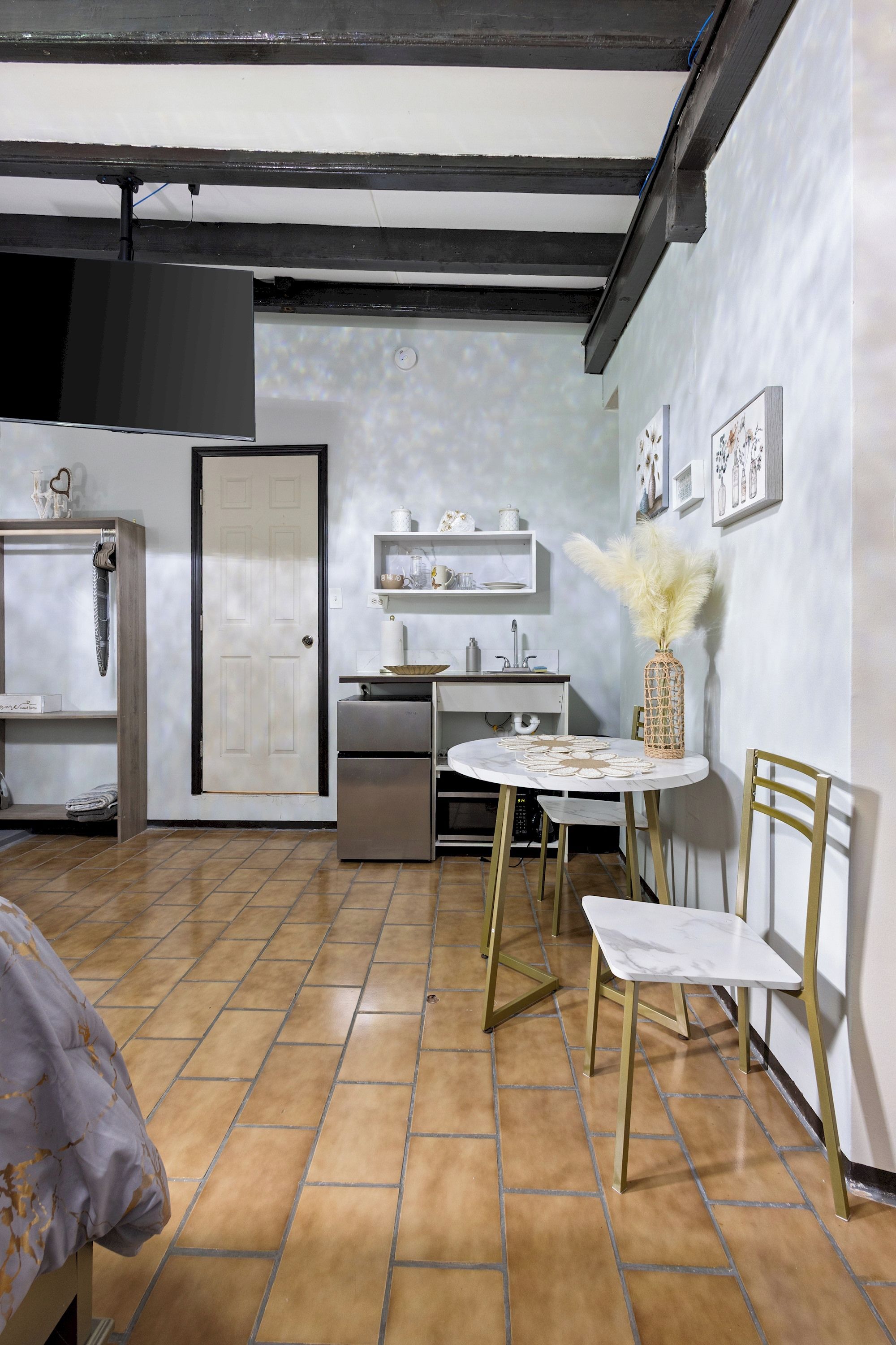 Cocina pequeña con refrigerador, pileta y muebles blancos. Se observa una mesa de comedor con sillas y un jarrón decorativo en la pared.