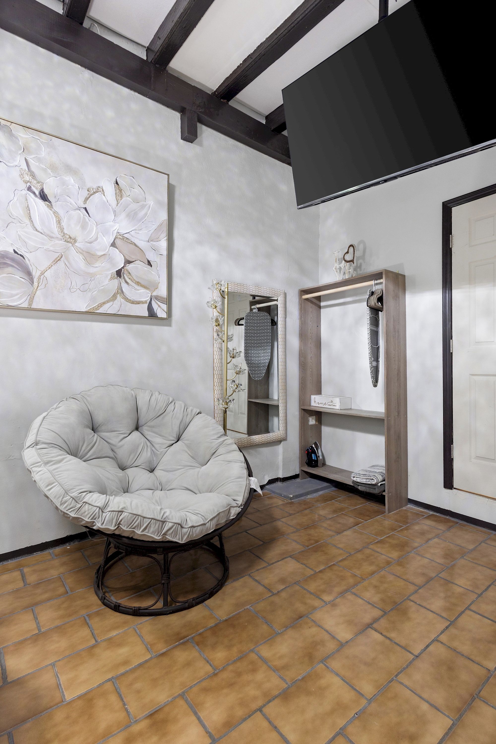 A room with a large, round, cushioned chair, a wall-mounted mirror with a decorative frame, and a shelving unit with various items.