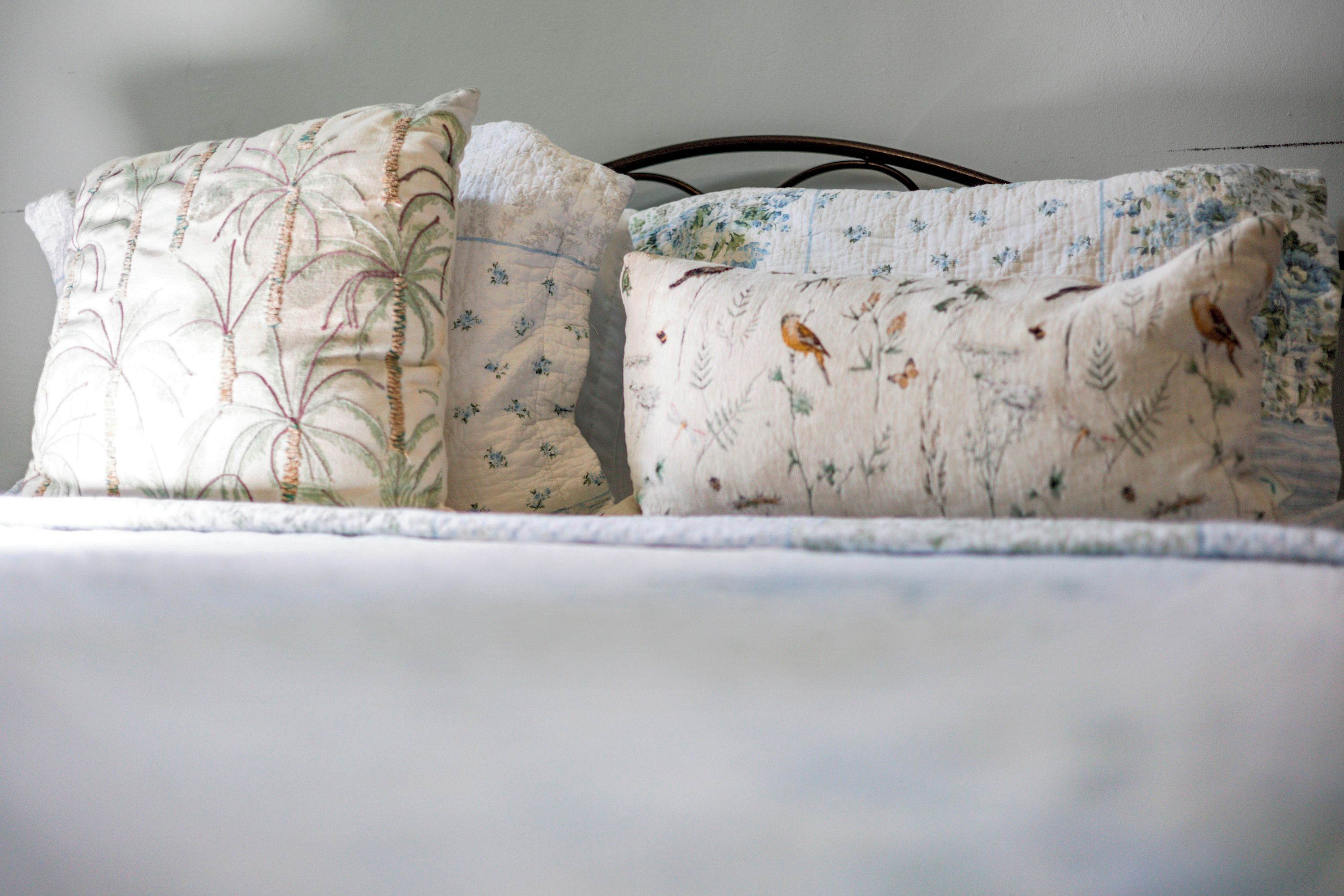 Una cama con dos almohadas, una con estampado floral y la otra con pájaros.