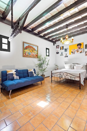 A room with a blue sofa, a bed with a white bedspread, a painting on the wall, and a chandelier. - The PR Suite at Casa of Essence | Old San Juan Encanto (San Juan)