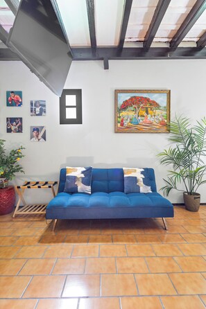 Une pièce avec un canapé bleu, un tableau et une plante en pot.