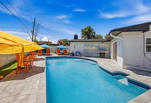 A swimming pool with lounge chairs and umbrellas, surrounded by a fenced yard and a building. - Bradenton Escape w/ Fire Pit, Pool & Putting Green (Bradenton)