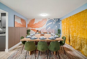 A dining area with a long table set for six, surrounded by green chairs, with a colorful abstract mural on the wall behind. - Bradenton Escape w/ Fire Pit, Pool & Putting Green (Bradenton)