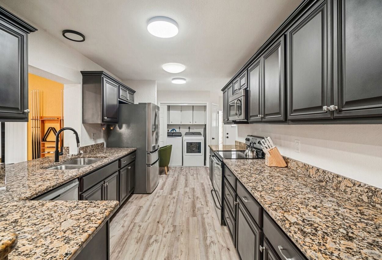 A kitchen with granite countertops, dark cabinetry, and a central island with a sink.