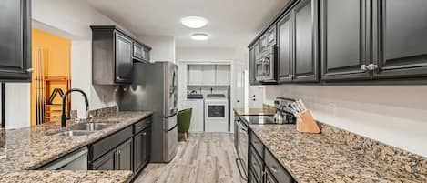 A kitchen with granite countertops, dark cabinetry, and a central island with a sink.