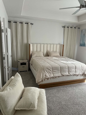 Een slaapkamer met een bed, nachtkastjes, een bankje en een plafondventilator.
