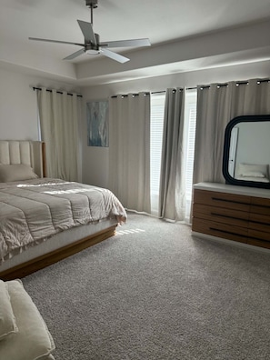 Een slaapkamer met een bed, een dressoir, een plafondventilator en een raam met gordijnen.