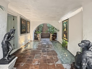 A hallway with a tiled floor, statues, framed artwork, and a staircase leading to a garden area. - Villa Oasis del Cielo · Vista al Lago y Montaña (Valle de Bravo)