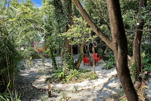 An outdoor seating area with red chairs and tables, surrounded by dense foliage and trees. - Villa Oasis del Cielo · Vista al Lago y Montaña (Valle de Bravo)