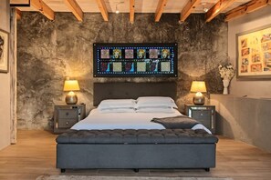 Une chambre avec un grand lit, deux tables de chevet avec des lampes, une œuvre d’art murale au-dessus du lit et un mur à texture.