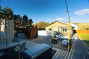 En udendørs patio med spisebord og stole, et overdækket siddeområde og et hus i baggrunden.