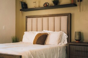 A neatly made bed with a wooden headboard, a bedside table with a lamp, and a shelf with books and decorative items. - Private Zion Stay HotTub~Pool~FirePit~Grill+Views (Colorado City)