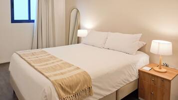 A hotel room with a bed, bedside table, lamp, and a window with curtains.