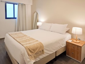 Hotellihuone, jossa on sänky, yöpöytä, lamppu ja ikkuna, jossa on verhot.