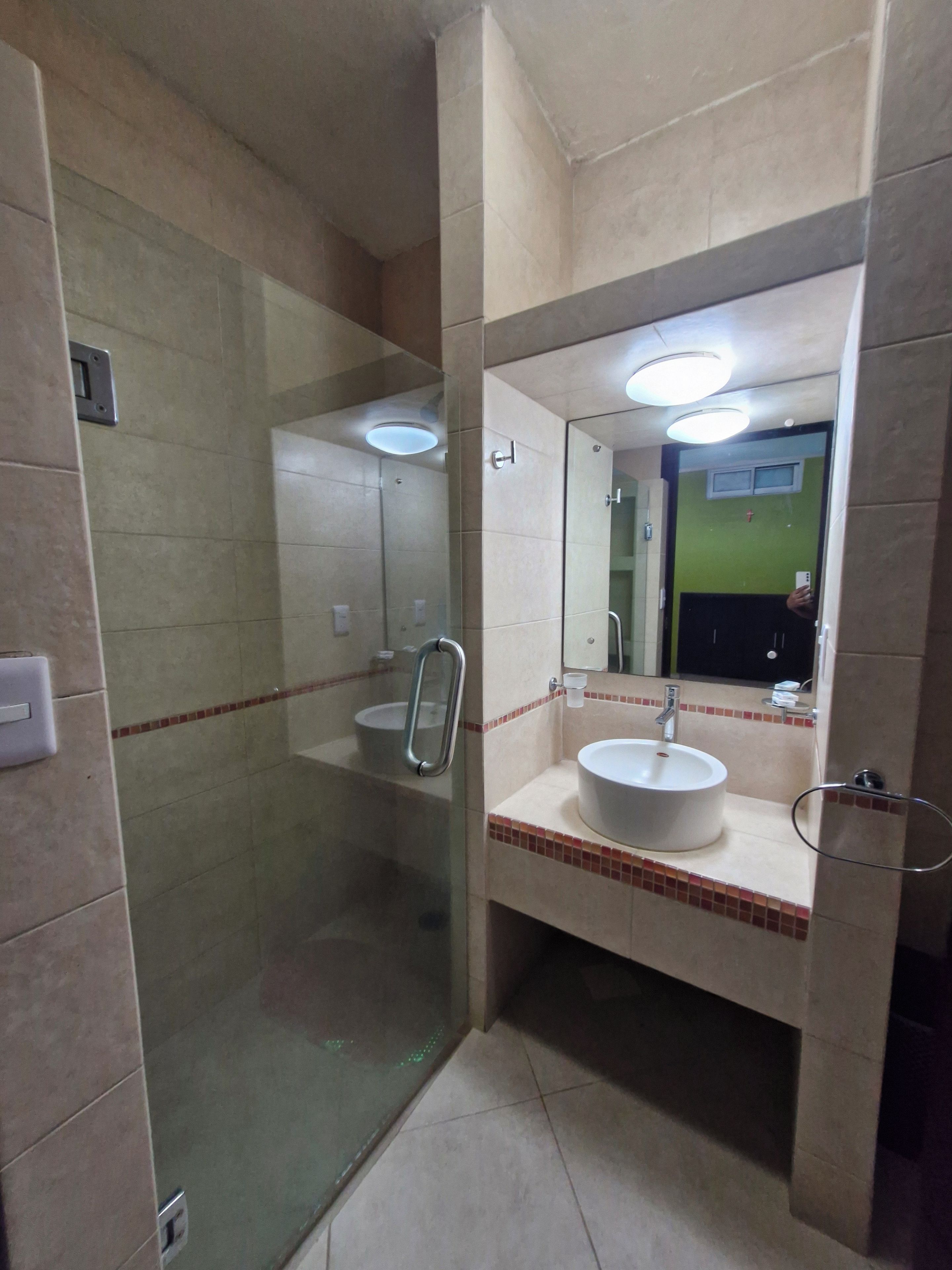 Un baño con ducha envuelta en vidrio, un lavamanos con espejo y un perchero para toallas.