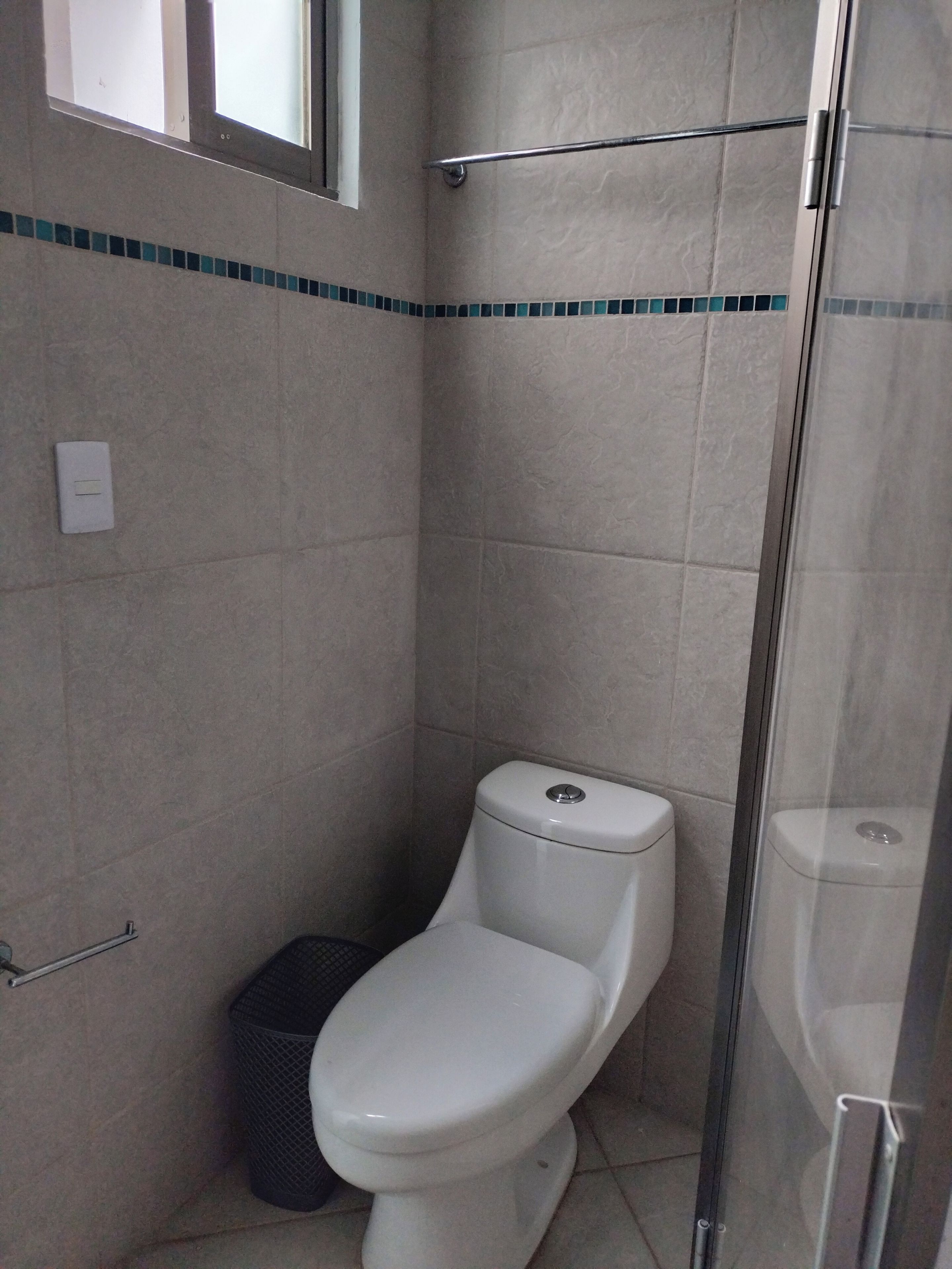Un baño pequeño y cerrado con inodoro, un cubo de basura y zona de ducha.