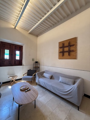 Un salon avec un canapé, une table basse, une œuvre d’art en bois accrochée au mur et une fenêtre avec des stores.