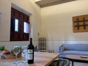 Een kamer met een eettafel, een fles wijn en een schaal met fruit.