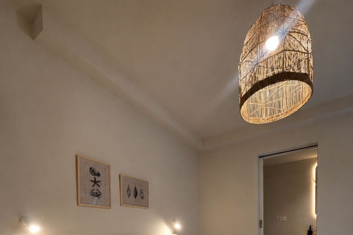 A hotel room with two beds, a woven light fixture, and artwork on the wall.