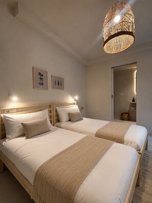 Quarto de hotel com duas camas, luminária de fibra natural e obras de arte na parede.