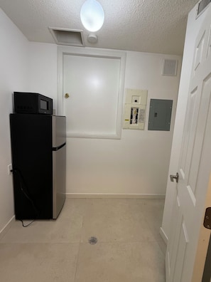 Una habitación pequeña y limpia con refrigerador, microondas y una puerta con cerradura.