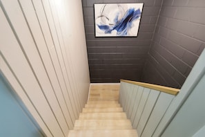 Un escalier avec des marches en bois et des rampes blanches, menant à un mur de briques sombres.