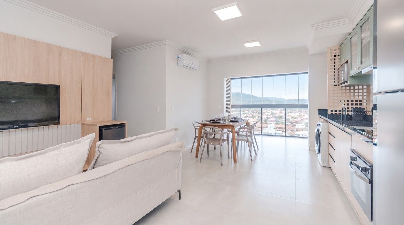 Ein modernes Wohnzimmer mit einer Couch, einem Essbereich mit Stühlen, einer Küche mit Geräten und einem großen Fenster mit Blick auf die Stadt.