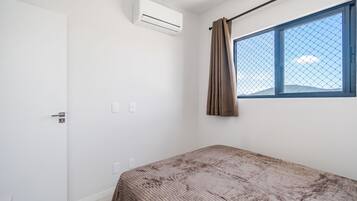 Een kamer met een bed, een raam met gordijn, een airconditioning en een deur.