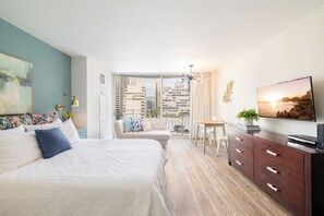 A modern bedroom with a large bed, a desk, a television, and a balcony with a city view. - 1095 Ilikai Marina Modern Studio Near Beach (Honolulu)