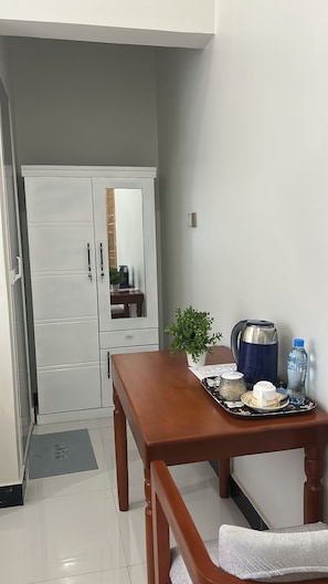 Uma área de refeições com uma mesa de madeira, uma garrafa de água, uma chaleira e uma pequena planta em vaso.