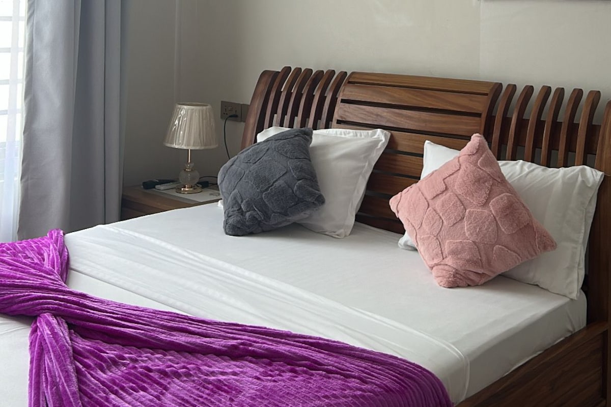 Quarto de hotel com cama, luminária de cabeceira, janela com cortinas e ar condicionado.