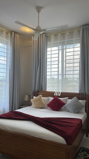 Quarto de hotel com cama, cortinas, ventilador de teto e janela com vista.