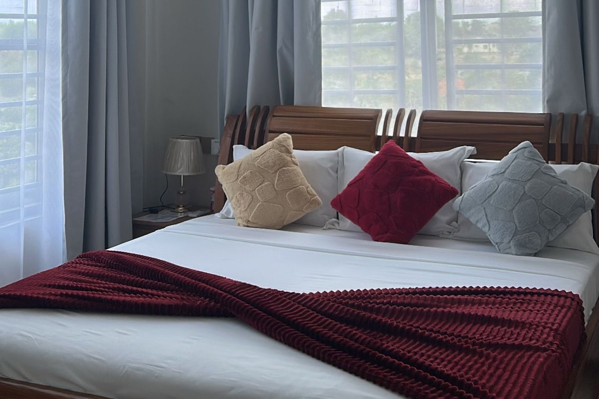 Quarto de hotel com cama, ventilador de teto e grandes janelas com cortinas.