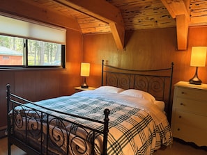Ein Schlafzimmer mit Holzwänden, einem Metallbettgestell, zwei Nachttischlampen und einem Fenster mit Jalousien.