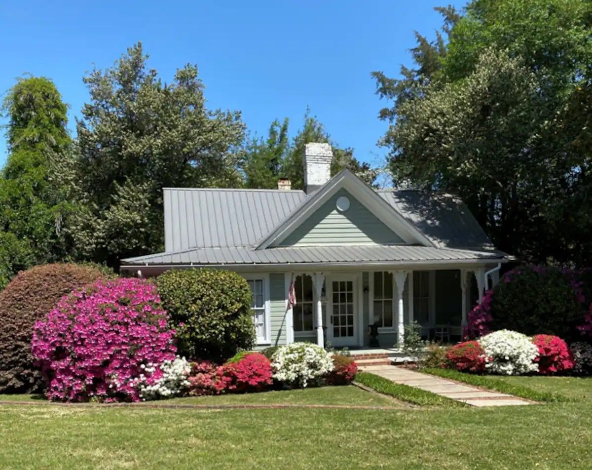 A house with a porch, surrounded by well-maintained gardens and trees.