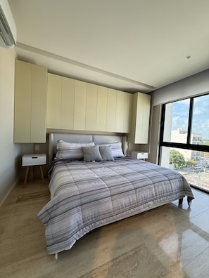 Une chambre dotée d’un grand lit, d’une armoire intégrée, de tables de chevet et offrant une vue sur l’extérieur grâce à une grande fenêtre.