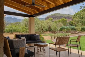 Ein Außenbereich mit einer Sitzecke, einschließlich einer Couch, Stühlen und einem Tisch, mit Blick auf einen angelegten Garten und Berge.