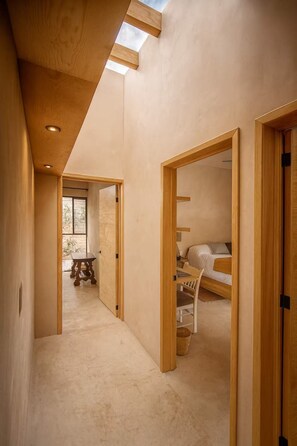 Ein schmaler Flur mit Holztüren, der zu einem Schlafzimmer mit Bett und Schreibtisch führt.