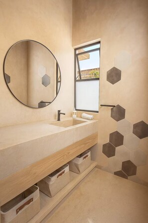 Un baño moderno con lavamanos doble, un espejo redondo y azulejos hexagonales en la pared.