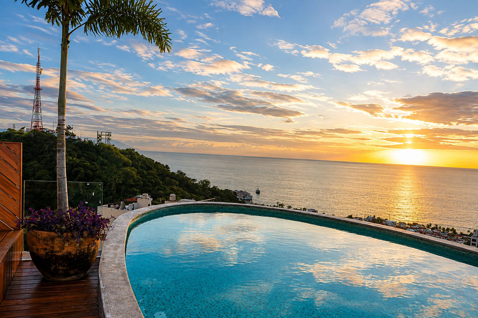 A curved infinity pool with a view of the sunset over the sea, surrounded by greenery and a wooden deck.